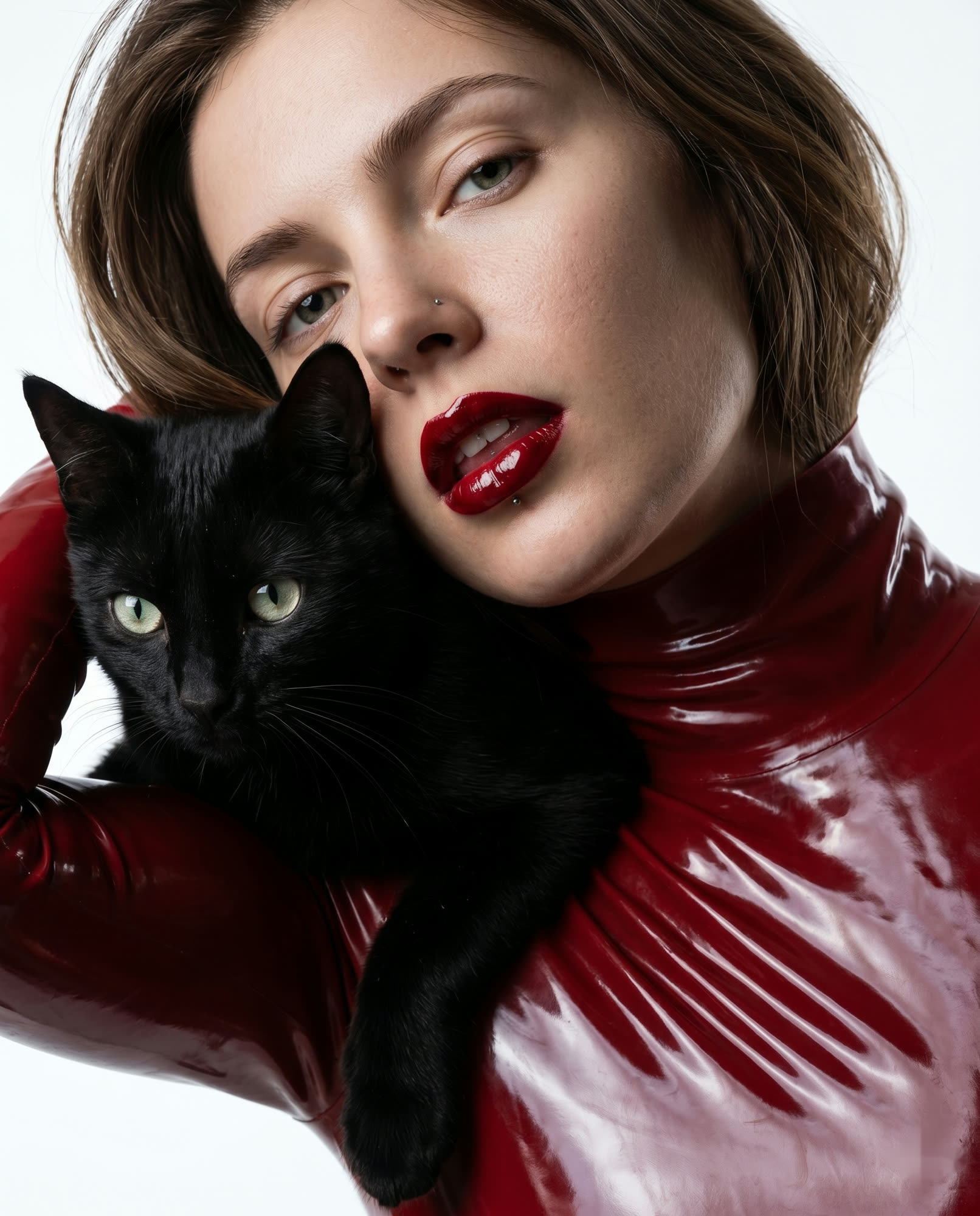 Ritratto beauty: modella con rossetto bordeaux e dolcevita in latex tiene un gatto nero sulla spalla
